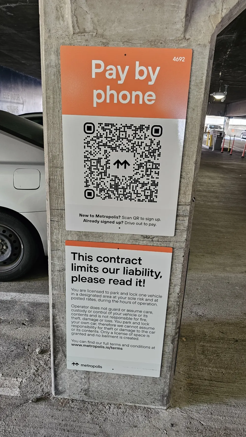 The Pay by phone sign posted on a pillar inside the Mercy General Hospital parking garage: an orange panel reading Pay by phone above a Metropolis QR code, with the line New to Metropolis? Scan QR to sign up. Already signed up? Drive out to pay.